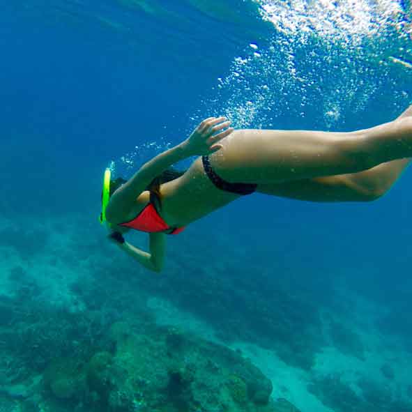 Eine Frau im Bikini und Schnorchelausrüstung taucht im türkisblauen Wasser unter
